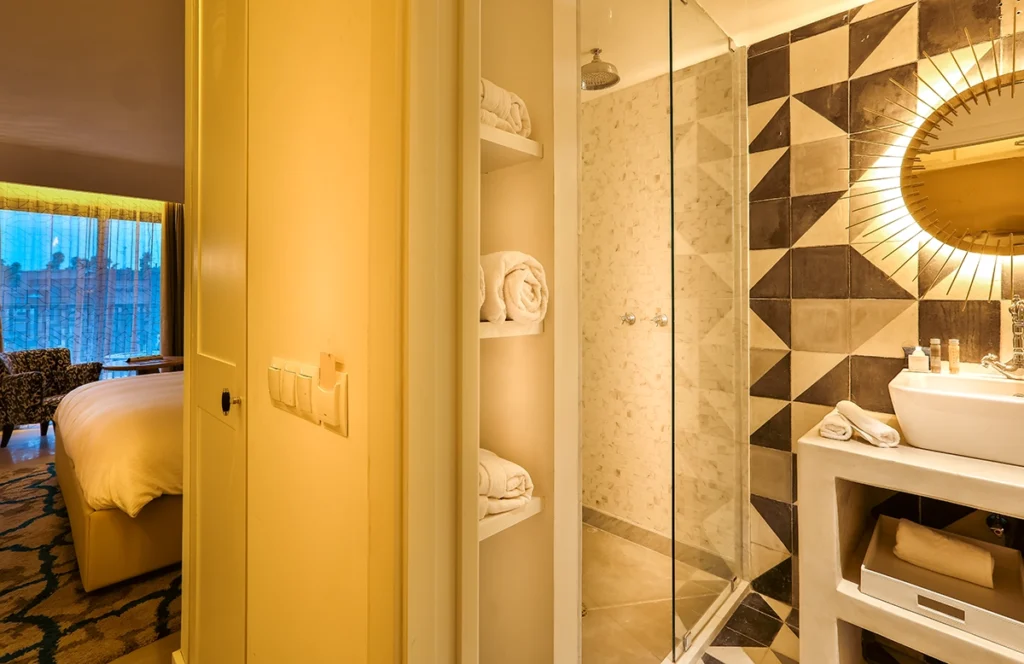 Baño de la habitación Deluxe del hotel 2Ciels Marrakech con ducha de cristal y espejo sol