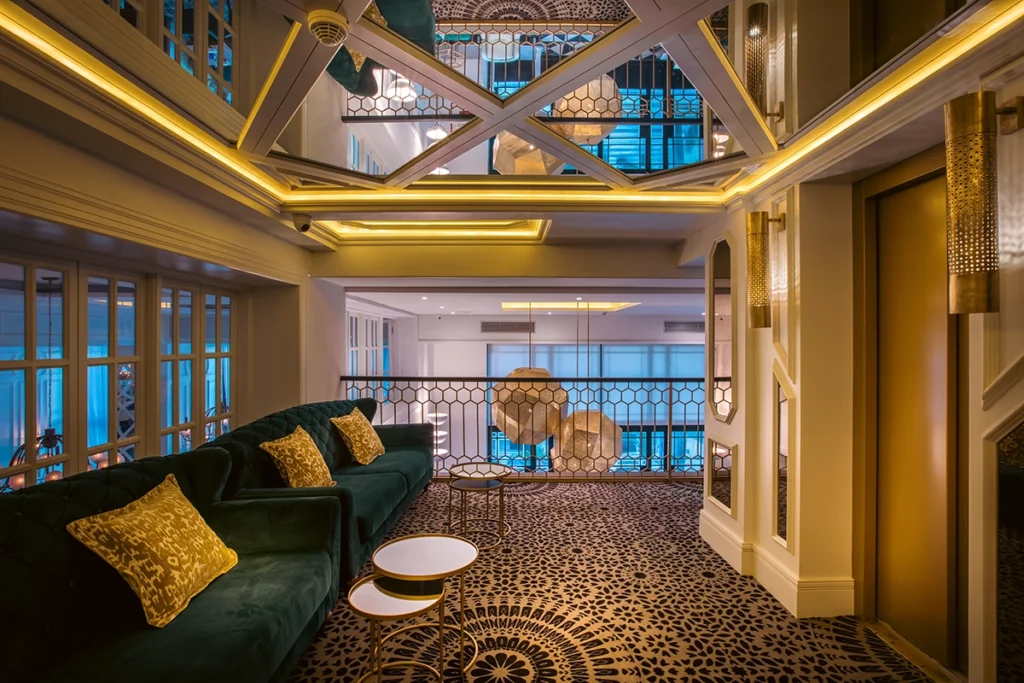 Salón junto al ascensor del hotel 2Ciels Marrakech con sofá de terciopelo verde y lámparas doradas