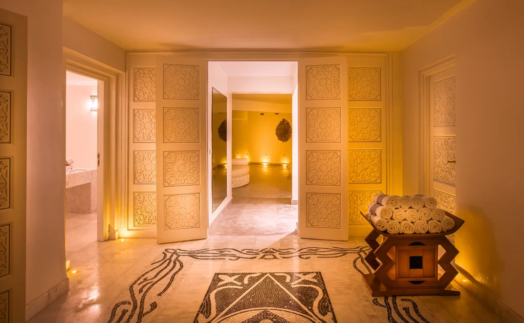 Pasillo del spa del hotel 2Ciels Marrakech con puertas talladas y suelo de mosaico
