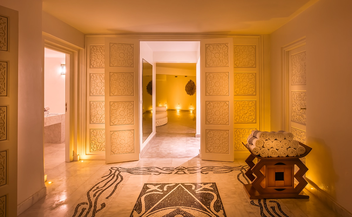 Pasillo del spa del hotel 2Ciels Marrakech con puertas talladas y suelo de mosaico